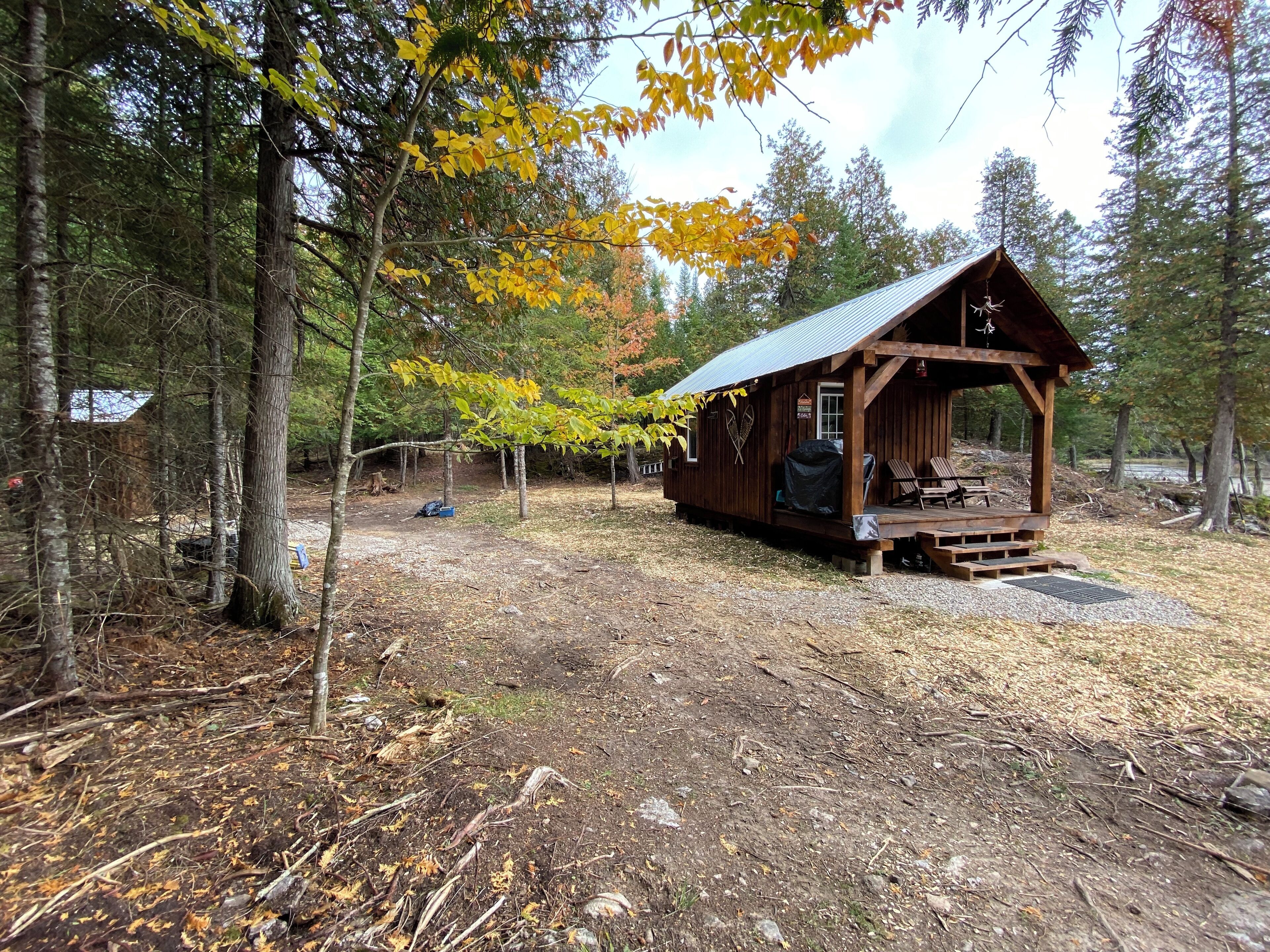 A rustic cabin with a porch, surrounded by trees with autumn foliage.