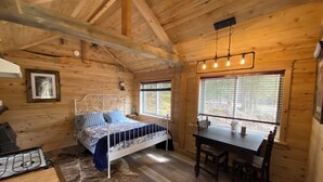 A wooden cabin interior with a bed, a dining table, and a stove.