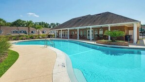 En swimmingpool med klart, blåt vand, omgivet af liggestole og en overdækket patio.