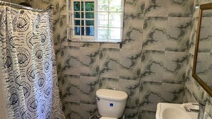 A bathroom with a patterned shower curtain, a toilet, a sink, and a window with a view of greenery. - 6-bedroom studio in welcoming Ocho Rios with WiFi, AC Escape to Tranquility (Ocho Rios)