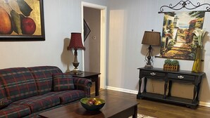 Ein Wohnzimmer mit einem Karomuster-Sofa, einem Couchtisch aus Holz, einem gemusterten Teppich, einem Konsolentisch mit Lampe und einem Bild an der Wand.