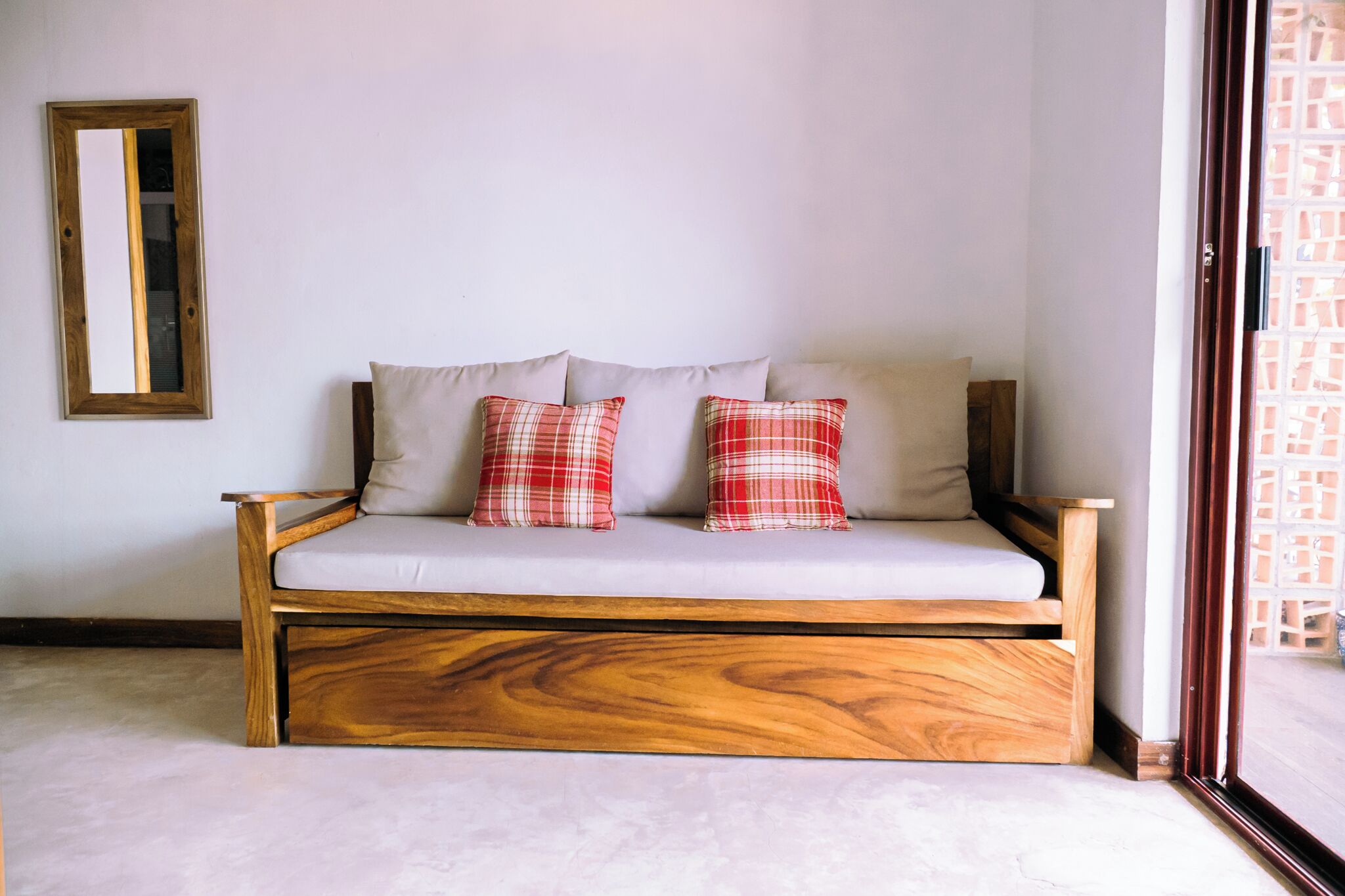 Un canapé en bois avec un coussin de couleur claire et deux oreillers à carreaux, le tout placé devant un mur uni.