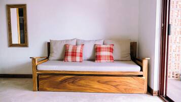 Un canapé en bois avec un coussin de couleur claire et deux oreillers à carreaux, le tout placé devant un mur uni.