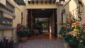 Entrada de hotel com arco de madeira, placa e plantas em vasos.
