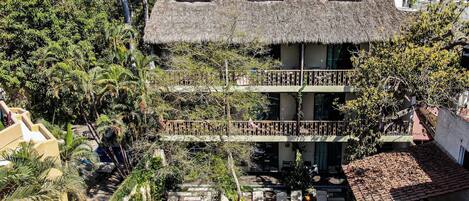 A two-story building with a pool, surrounded by lush greenery and palm trees.
