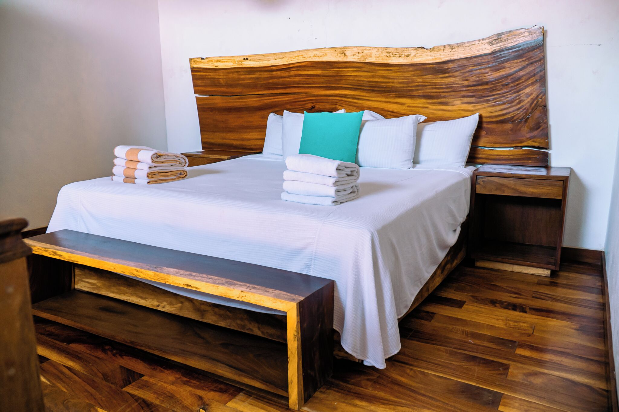 Un letto rifatto con cura, con una testiera in legno, un comodino e una panca ai piedi del letto.