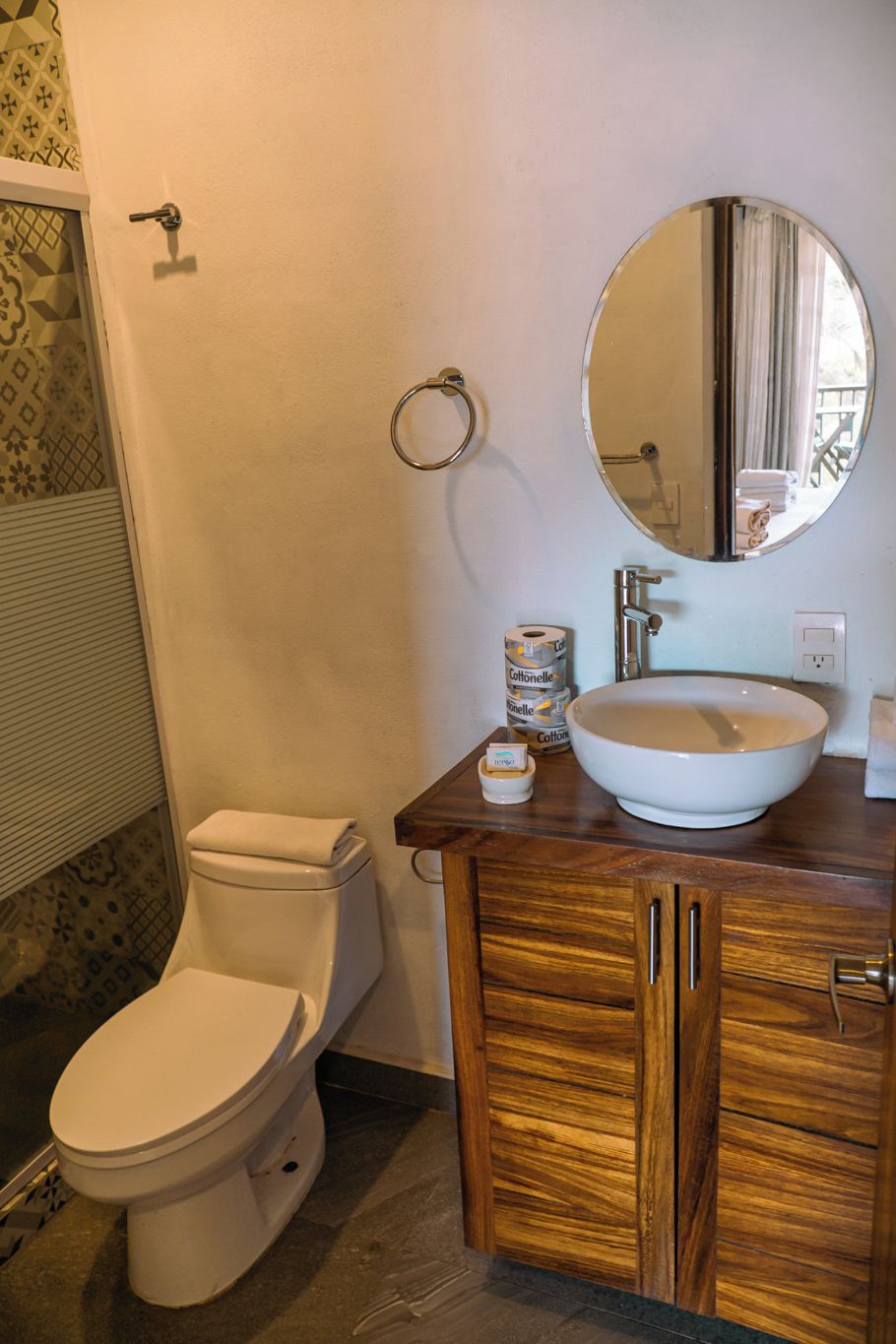 Un baño con un inodoro blanco, un tocador de madera con un espejo grande y un lavabo blanco.