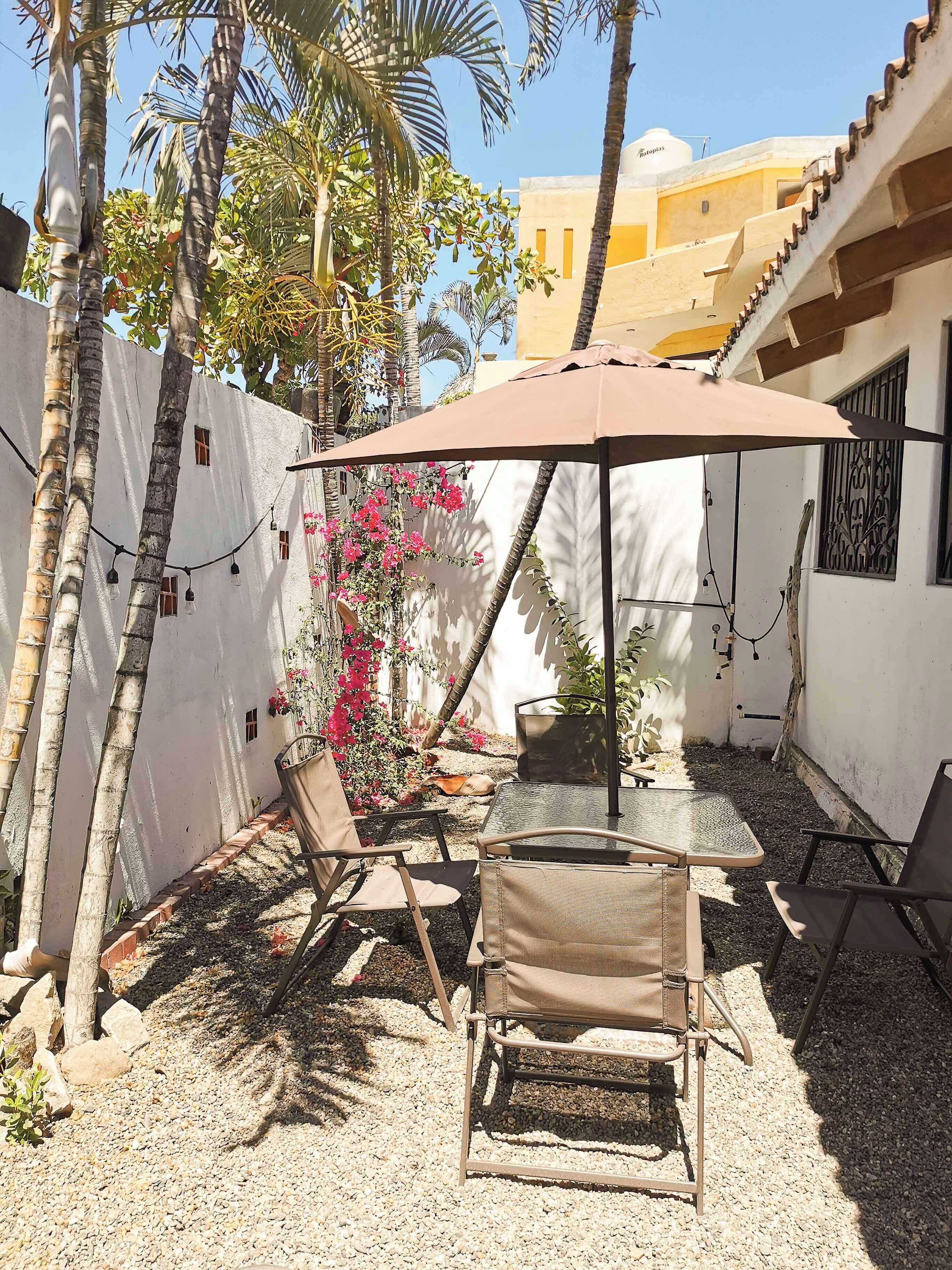 A patio area with a table and chairs, surrounded by a white wall and palm trees.