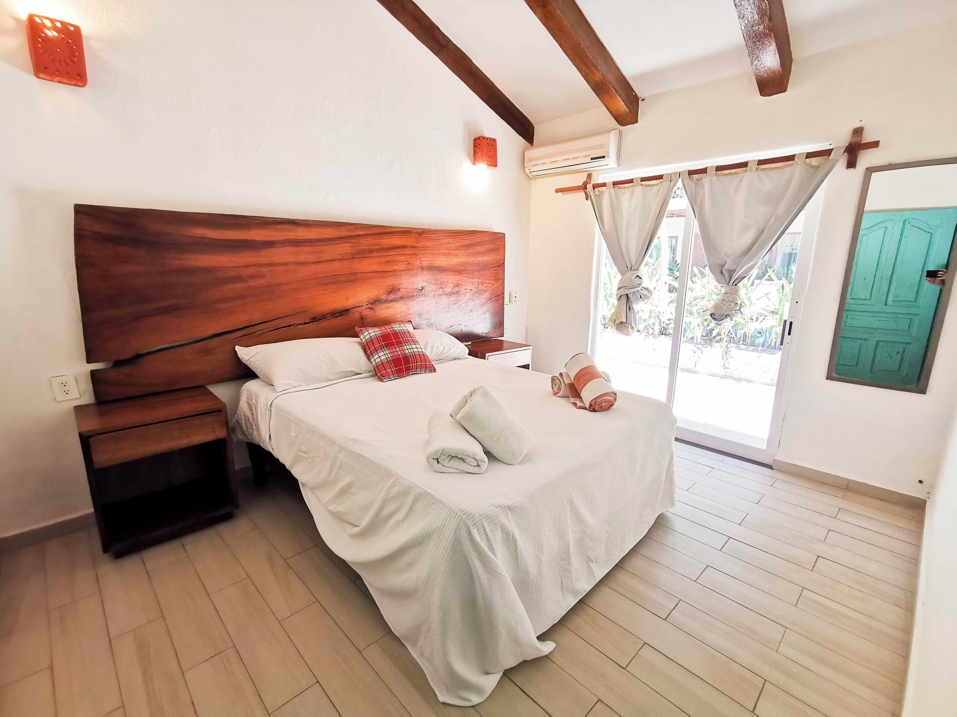 A bedroom with a wooden headboard, a bed with white bedding, a nightstand, and a window with curtains.