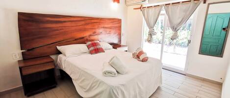 A bedroom with a wooden headboard, a bed with white bedding, a nightstand, and a window with curtains.
