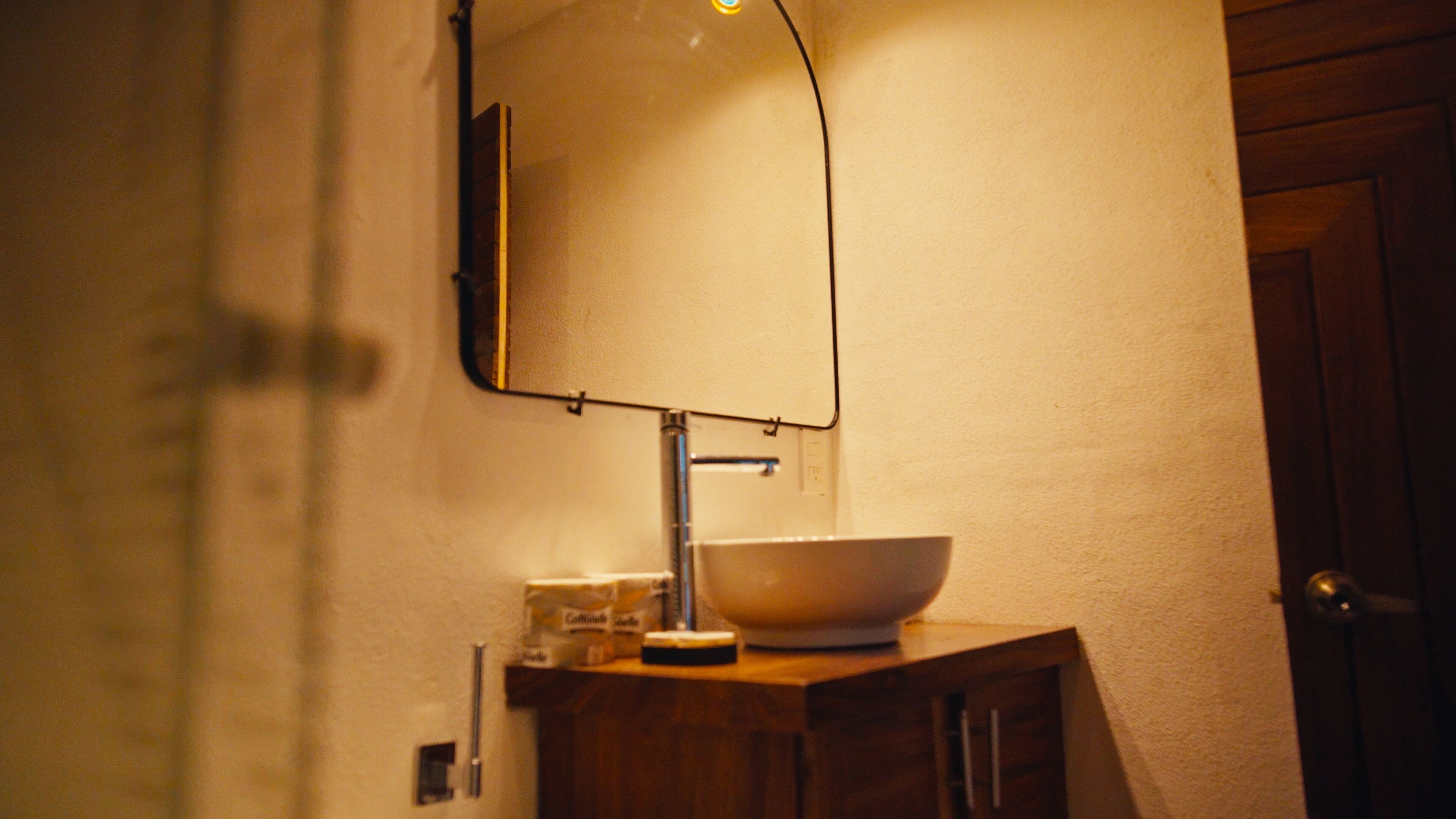 Un baño con lavamanos blanco, un espejo y un armario de madera.