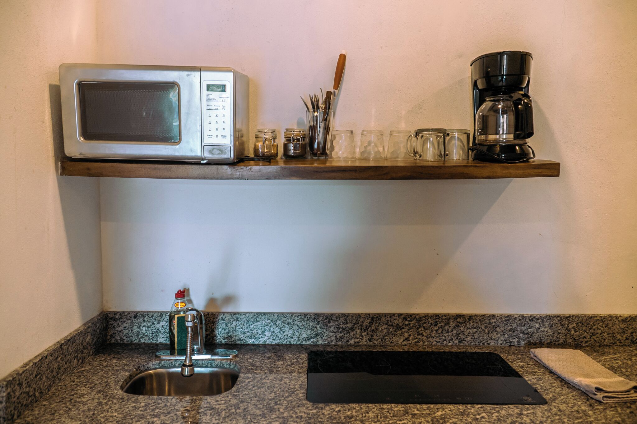 Una cocina equipada con microondas, cafetera y un estante con utensilios y vasos.