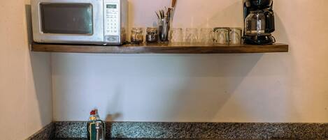 Una cocina equipada con microondas, cafetera y un estante con utensilios y vasos.