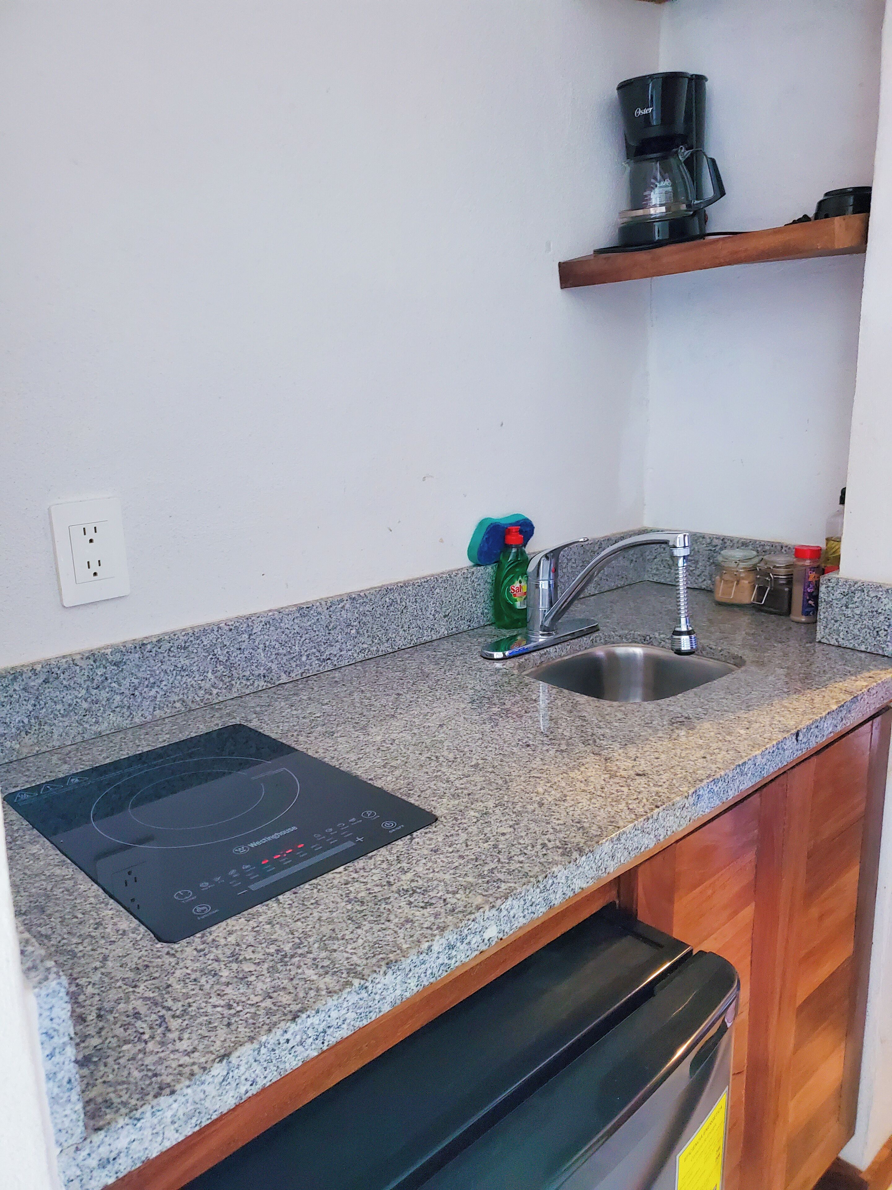 A kitchen with a built-in induction cooktop, a stainless steel sink, and a coffee maker on a shelf.