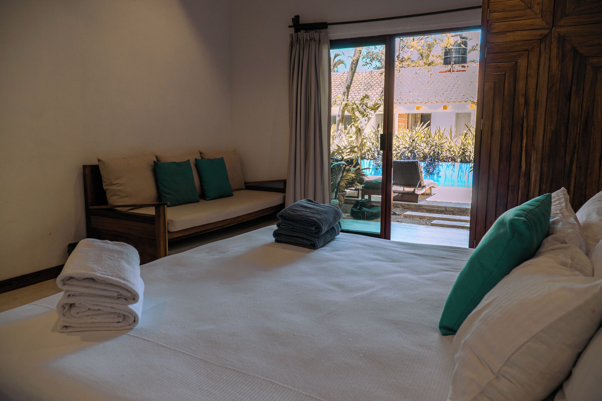 Habitación de hotel con cama, sofá y vistas a una piscina y follaje.