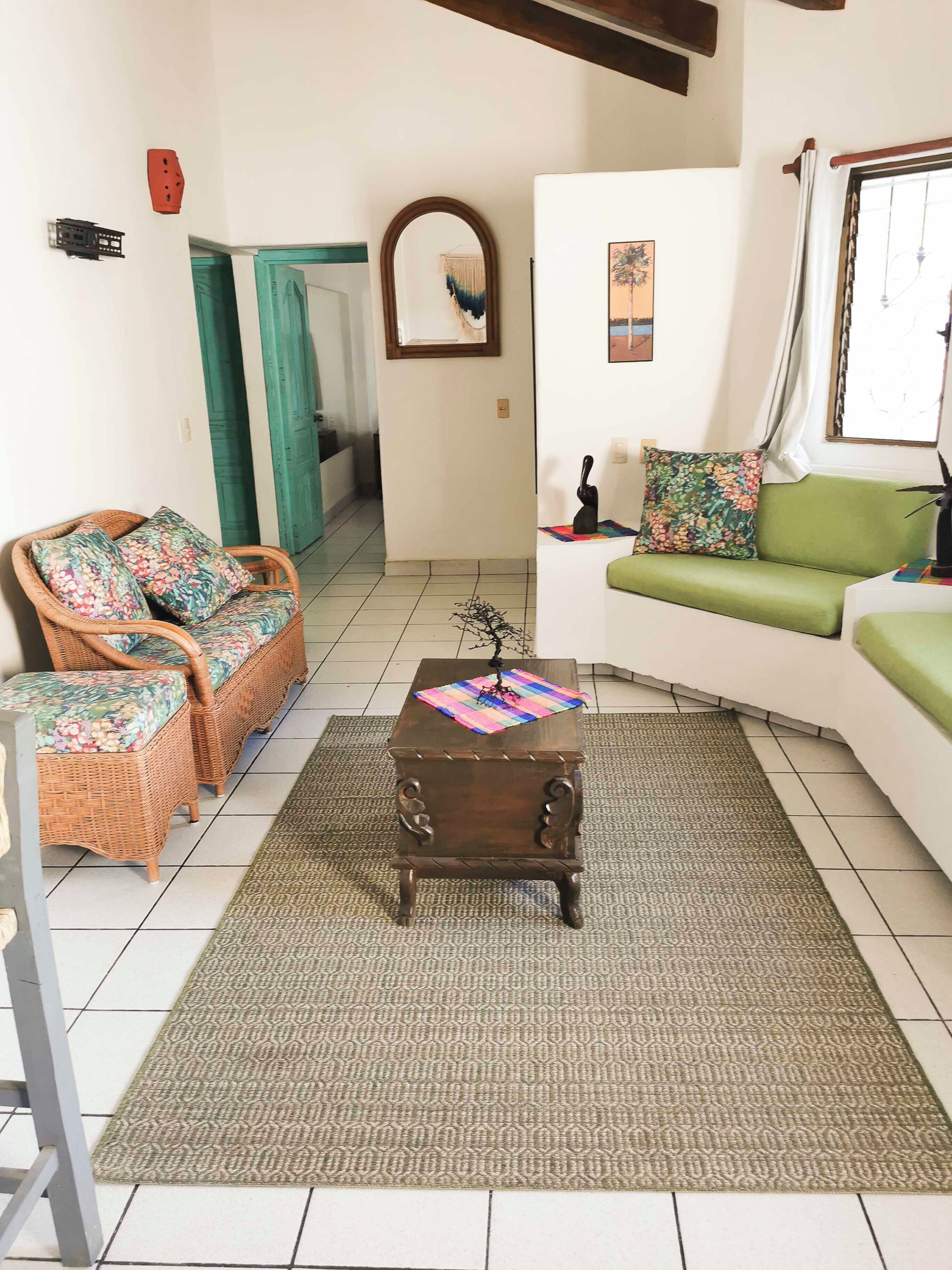 A living room with a green sofa, a wicker sofa with floral cushions, a wooden coffee table, and a patterned rug.