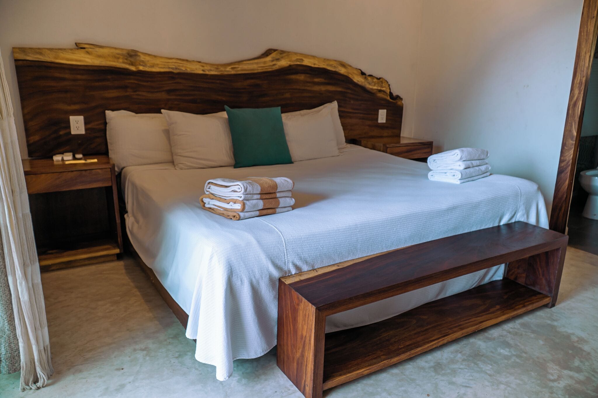 A bedroom with a large bed, wooden headboard, two bedside tables, and a bench.
