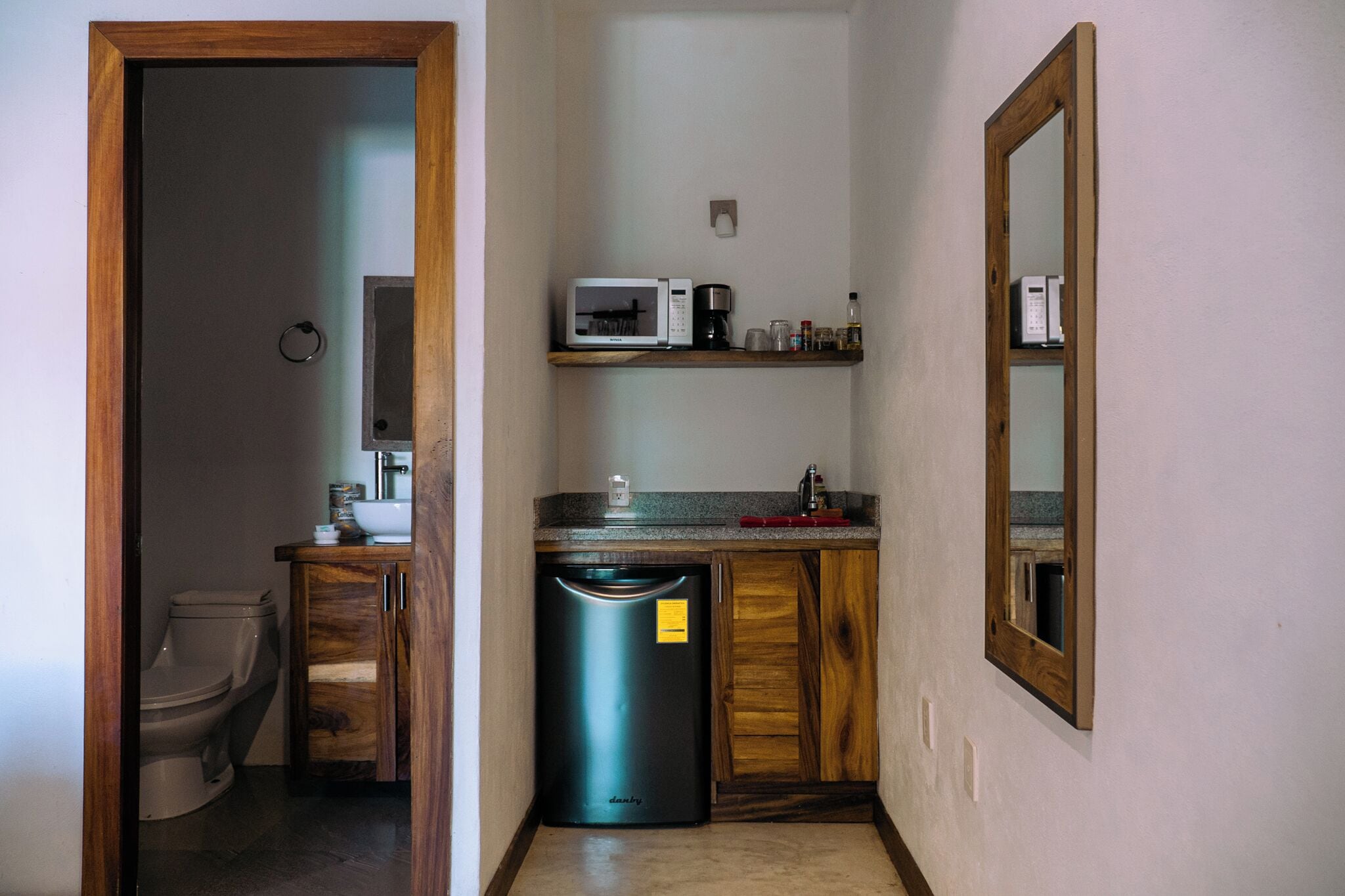Un baño pequeño con inodoro, lavamanos, espejo y un microondas en un estante.