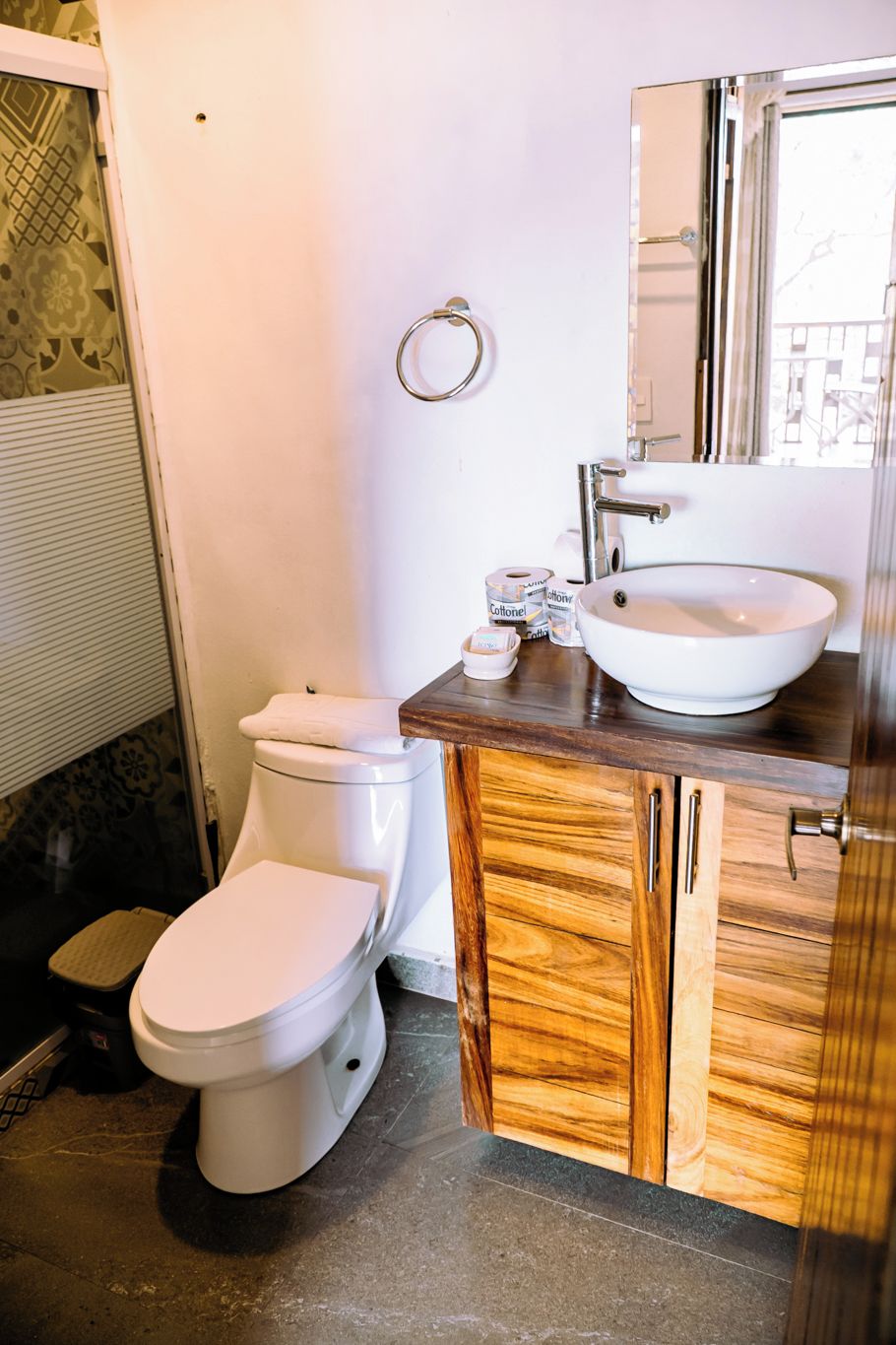 Un baño con inodoro blanco, tocador de madera con lavabo y espejo.