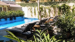 Uma área à beira da piscina com espreguiçadeiras e plantas em vasos.