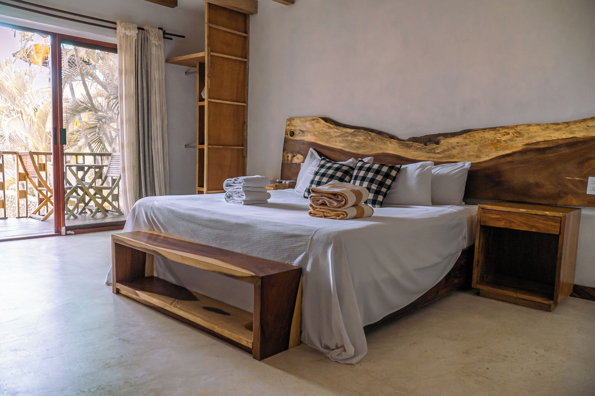 Un dormitorio con una cama grande, cabecera de madera y un banco. Hay una mesita de noche de madera y una estantería.