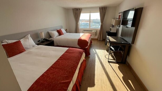Ein Hotelzimmer mit zwei Betten, einem Schreibtisch, einem Fernseher und einem Fenster mit Vorhängen.