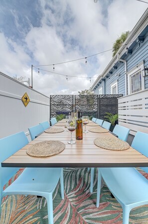 Un espace de restauration en plein air avec une longue table en bois, des chaises bleues et un décor attrayant en arrière-plan.
