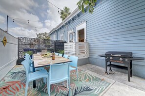 Une terrasse avec une table dressée pour quatre personnes, des chaises bleues, un barbecue et une clôture décorative.
