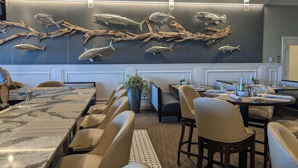 Un restaurant doté d’une longue table à manger, de nombreuses chaises et d’un mur décoré de motifs représentant des poissons et des branches.