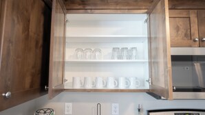 A kitchen with wooden cabinets, a stainless steel refrigerator, and a shelf with white mugs and glass jars.