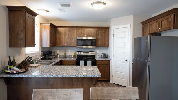 A kitchen with wooden cabinets, a stainless steel refrigerator, a microwave, an oven, and a granite countertop.