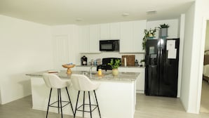 A modern kitchen with white cabinets, a black refrigerator, a microwave, and two bar stools. - Comfy Family Home w/ 4 rooms, WiFi, Office & Community Pool, in Rhome (Rhome)