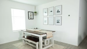 A room with a white wall, a wooden table with a bench, a window with blinds, and framed pictures on the wall. - Comfy Family Home w/ 4 rooms, WiFi, Office & Community Pool, in Rhome (Rhome)
