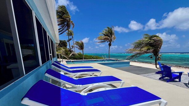 Un espace aménagé au bord de la piscine, avec des chaises longues bleues et une vue sur l’océan.