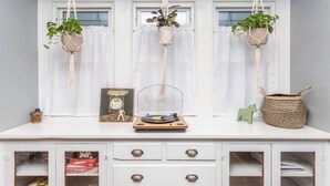 A white cabinet with three macrame plant hangers, a vinyl record player, and a Scrabble box.