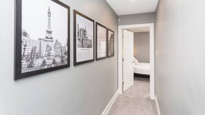 A hallway with framed black and white cityscape photos on the wall, leading to a bedroom with a bed and a nightstand.