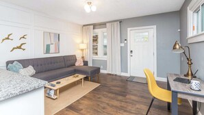 A modern living room with a grey sectional sofa, a yellow chair, a wooden coffee table, and a desk with a lamp.