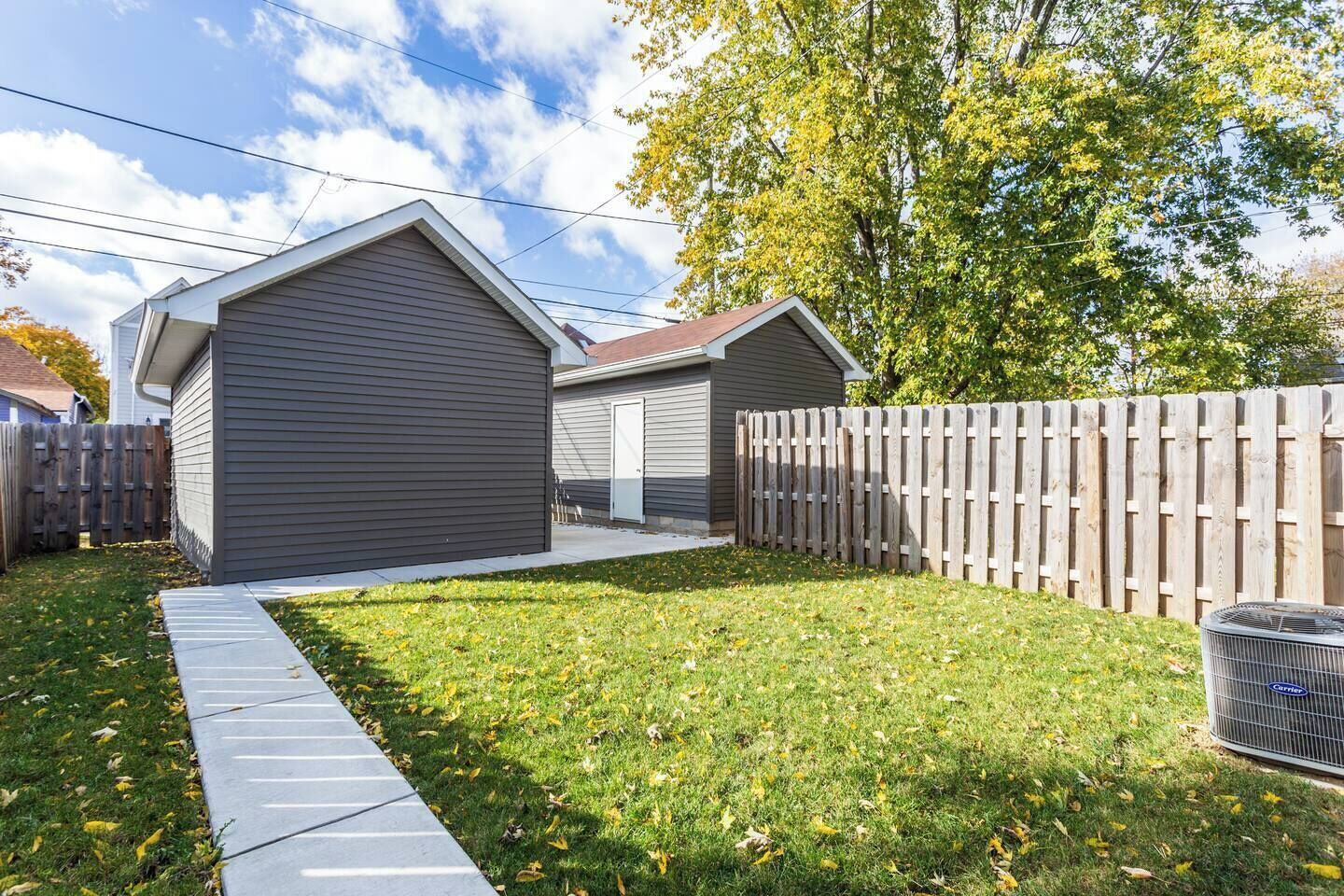 A residential property with a covered garage, a wooden fence, and a grassy yard.