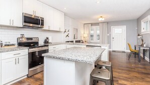 A modern kitchen with white cabinetry, stainless steel appliances, and a granite countertop island with stools.