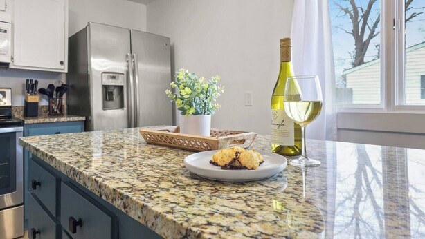 Una cocina con encimeras de granito, un refrigerador de acero inoxidable, una planta en maceta, una botella de vino y una copa de vino.