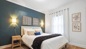 Un dormitorio con cama, mesitas de noche, una alfombra estampada y dos lámparas fijadas a la pared.