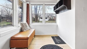 Habitación de esquina con techo de madera, un banco, repisa negra y vista a un patio trasero a través de amplias ventanas.