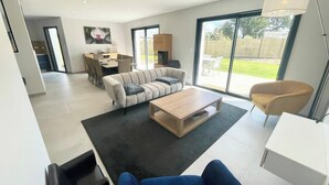 A modern living room with a sofa, coffee table, and a dining area with chairs. - Luxury Maison d'Architecte neuve de standing (Larmor-Baden)
