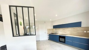 A modern kitchen with blue cabinets, a white countertop, and a tiled floor. - Luxury Maison d'Architecte neuve de standing (Larmor-Baden)