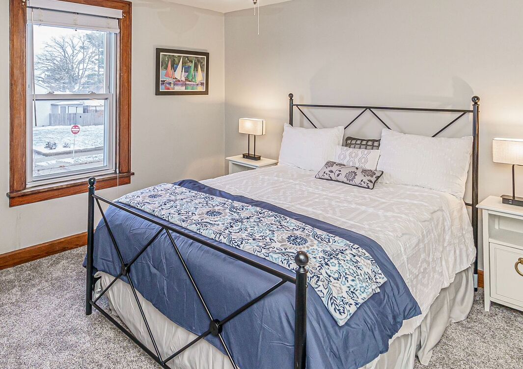 Un dormitorio con una cama, dos mesitas de noche, un ventanal y un cuadro en la pared.