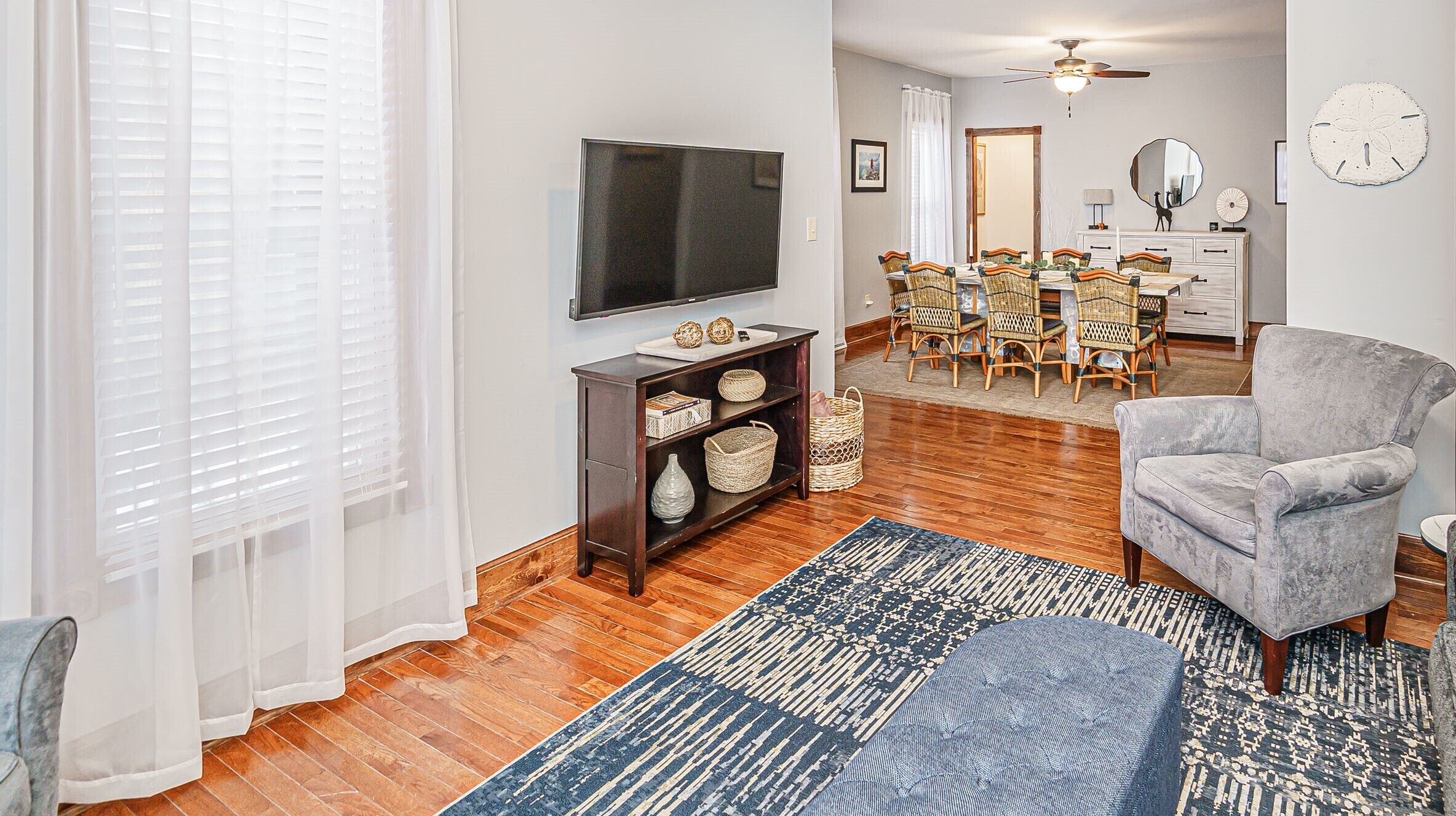 A living room with a TV, wicker chairs, a grey armchair, and a patterned rug.