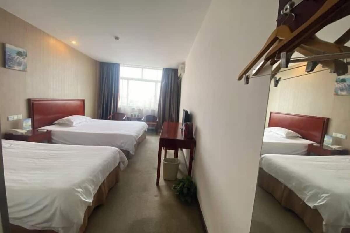 A hotel room with two single beds, a wooden nightstand with a lamp, a desk, and a chair.