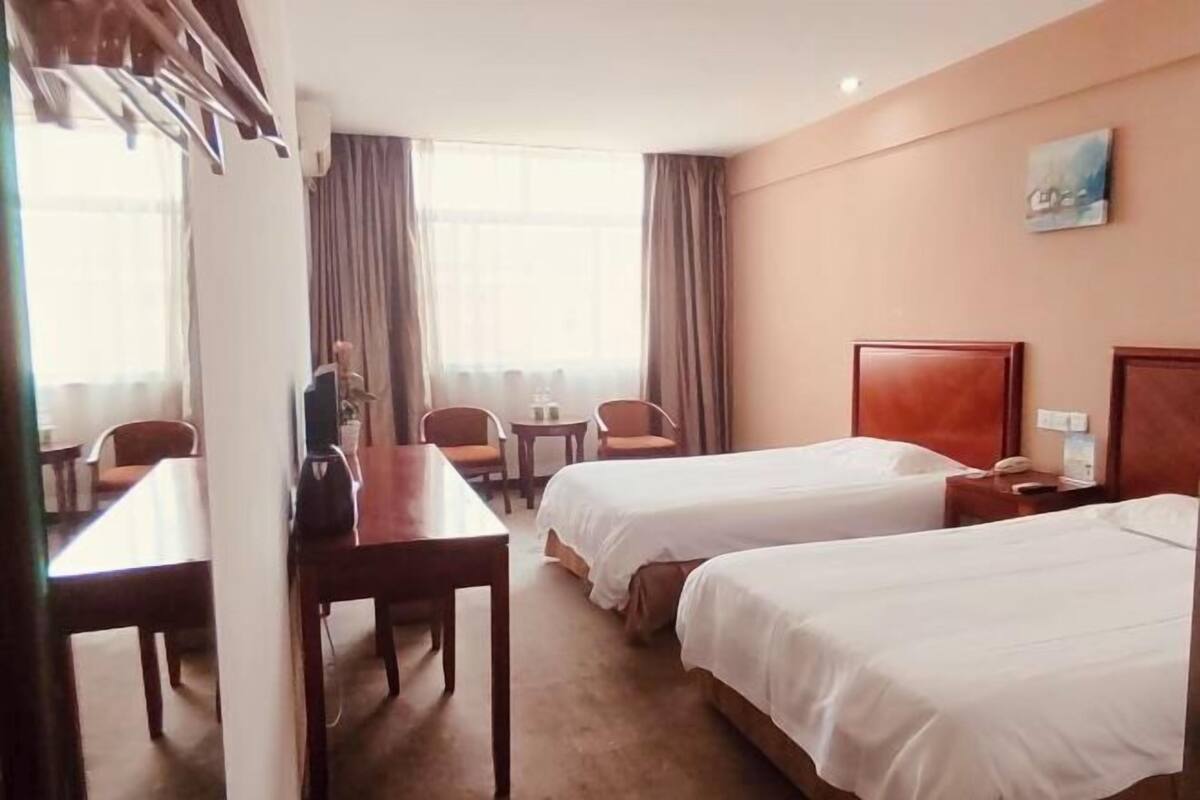A hotel room with two beds, a dining table, chairs, a small table with a lamp, and a painting on the wall.