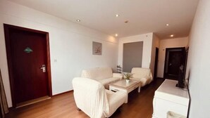 A room with a wooden floor, a sofa, a coffee table, a small table, a trash bin, and a door with a sign. - Green Tree Alliance Hotel (Shanghai East Jinxiu Road) (Shanghai)