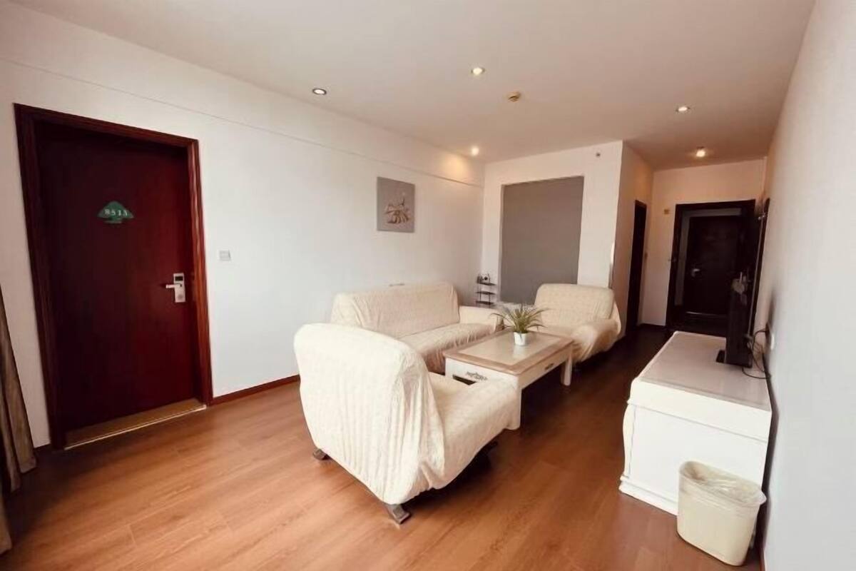 A room with a wooden floor, a sofa, a coffee table, a small table, a trash bin, and a door with a sign.